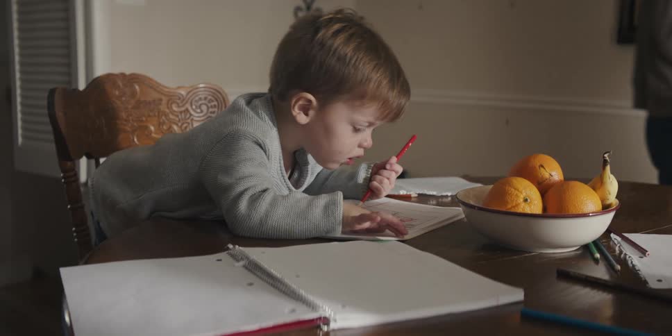 A mother and girl checking on a toddler boy coloring at a dining table