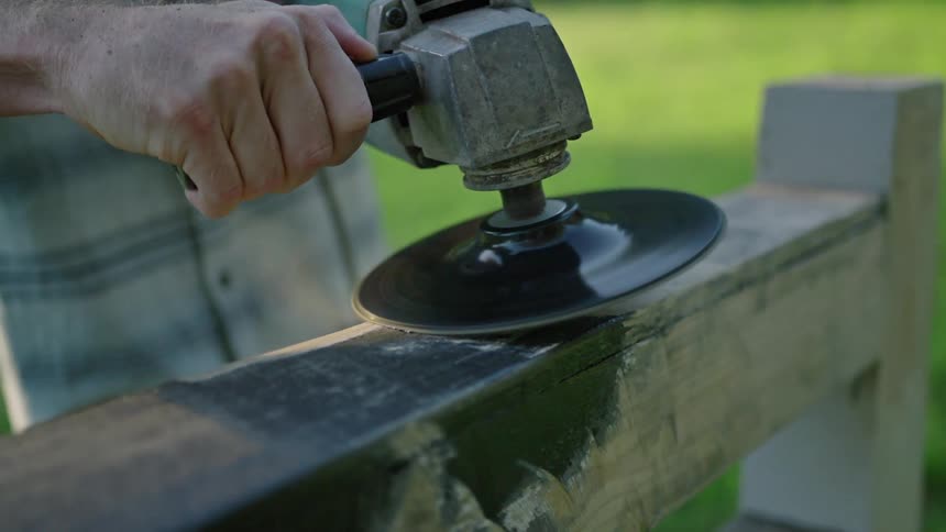 A person sands a wooden object outdoors