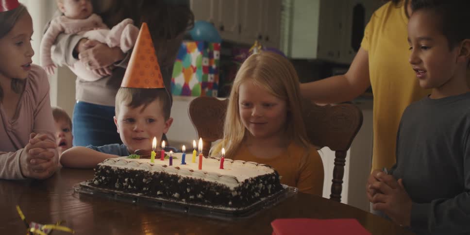 A little girl blows out the candles on her birthday cake surrounded by family and friends