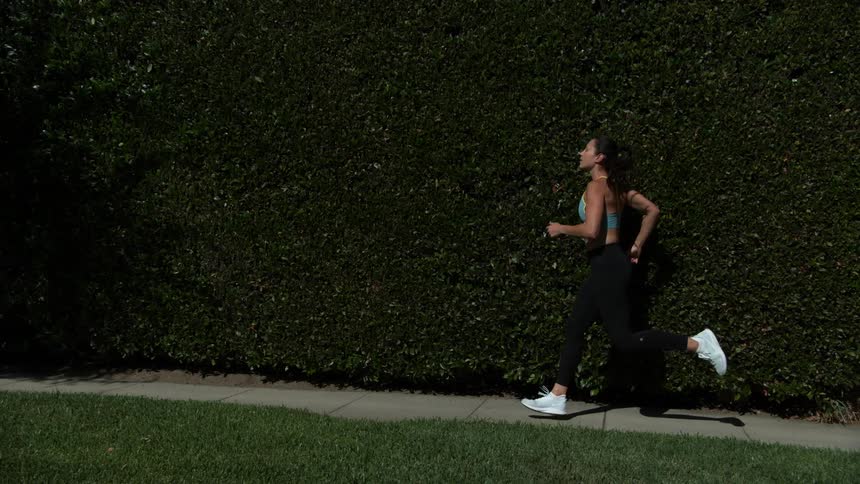 A woman in a sports bra jogging on an outdoor sidewalk in summer