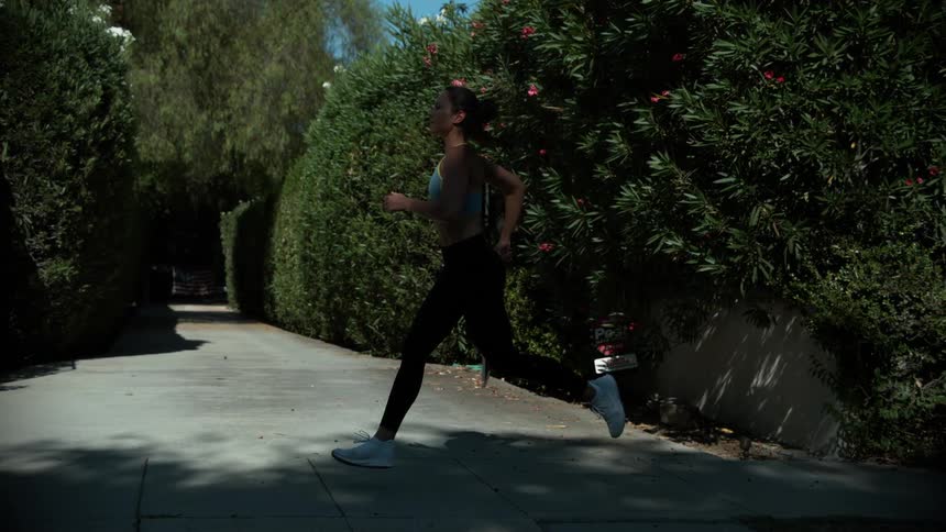 A woman in a sports bra jogging on an outdoor sidewalk