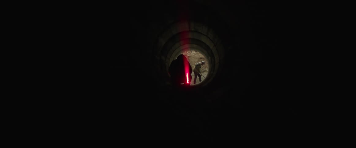 Silhouette of a construction worker using a laser to take measurements inside a subterranean pipe