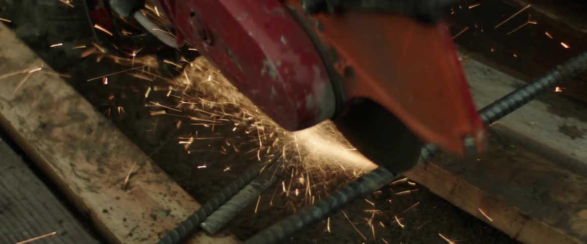 Metal saw sends out sparks as it cut through metal bar set across wood boards