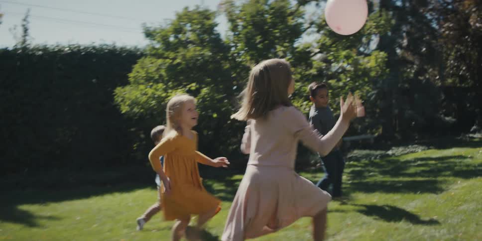 Four young children chasing and bouncing a balloon in a grassy backyard