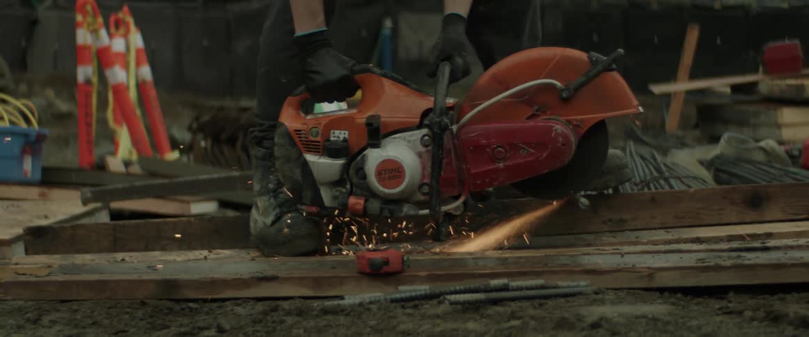 Worker wearing gloves makes sparks fly while cutting metal with a power tool on a construction site