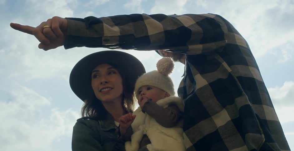 Father stands outdoors with wife and their child and points things out