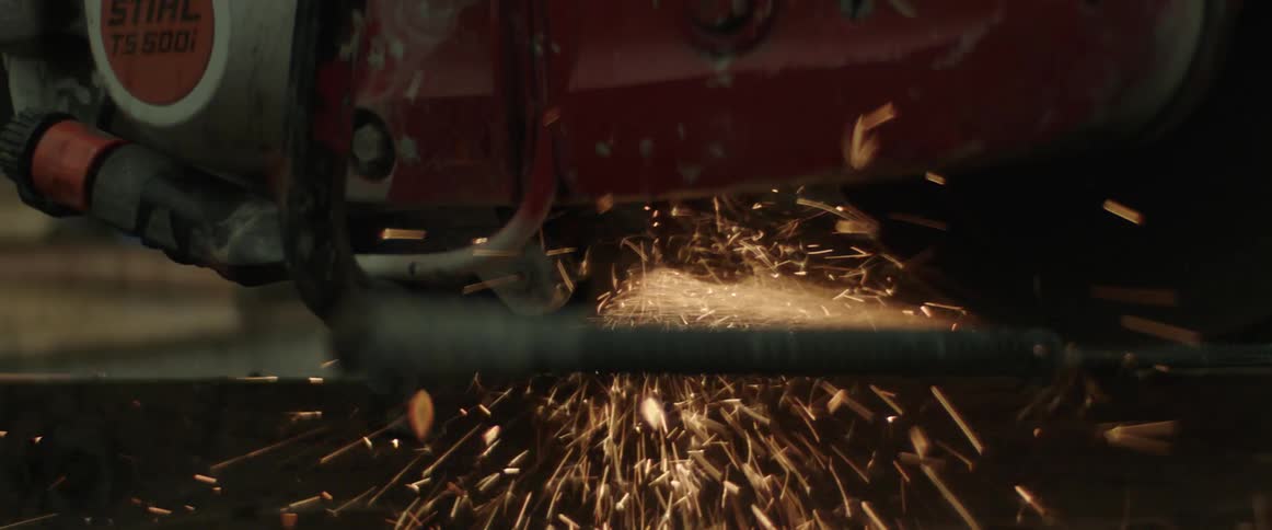 Worker makes sparks fly while cutting metal with a power tool on a construction site