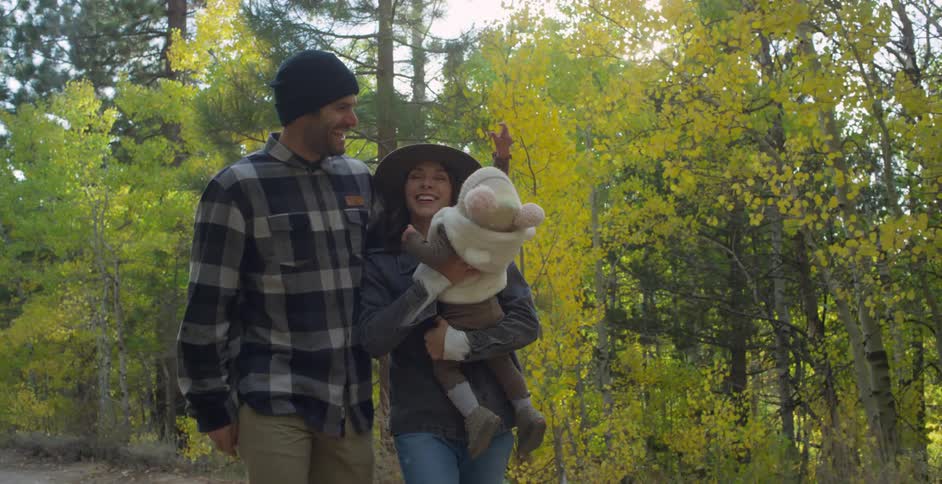 A man puts his arm around his wife as they walk a trail while she carries their daughter