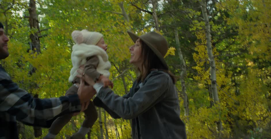 A father passing his young daughter to the mother while walking in a forest
