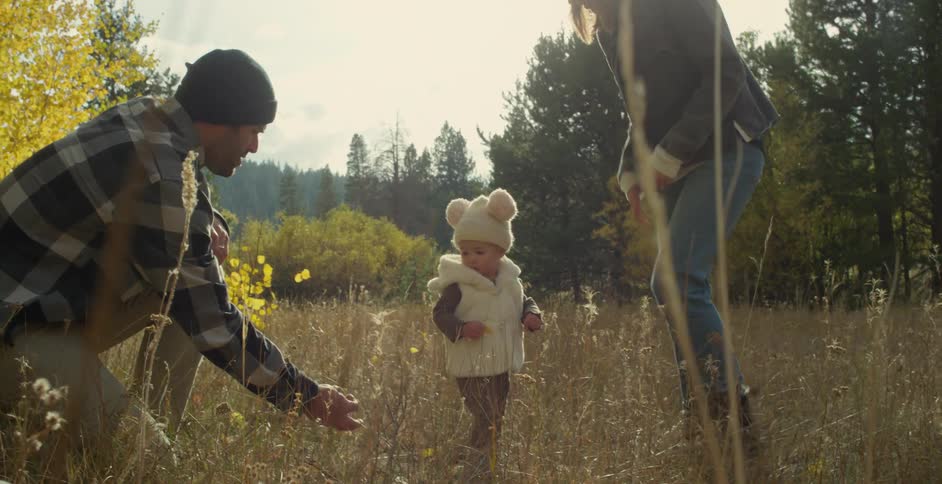 A father and mother with a young daughter in a grassy field on an autumn day
