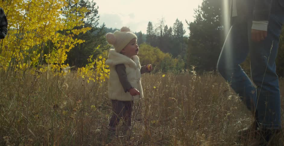 Mother walks around near daughter playing in field with forest in the background