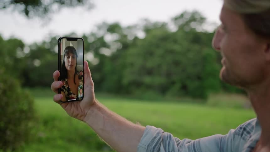 A man is standing outside holding his cell phone and having a video chat with a woman