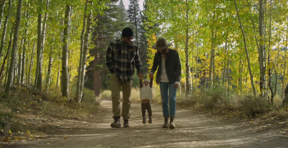 Mom and dad hold their little girls hands lifting her up as they walk a trail in the woods