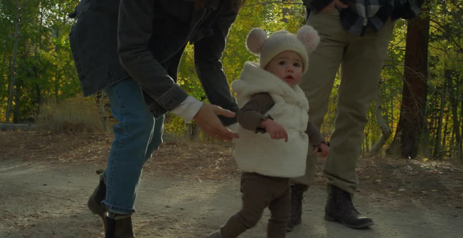A woman puts her daughter down to walk as they hike along a trail in the woods