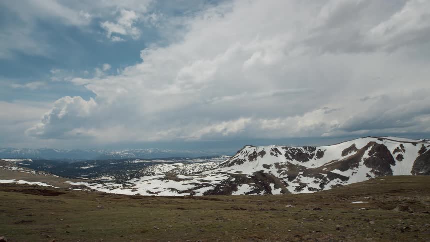 Clouds flow across sky casting shadows on plateau with view of snow covered mountains
