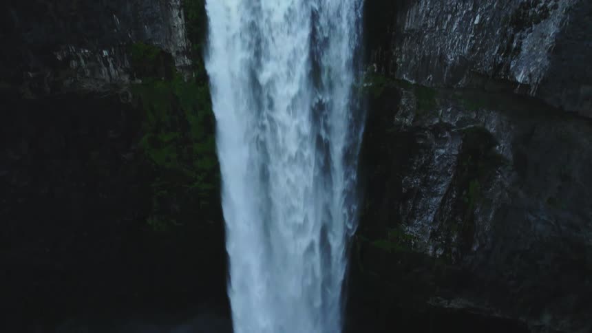 Aerial view of a strong waterfall pouring down a the rock face of a cliff on a lake in the mountains