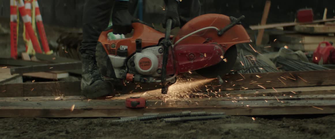 A construction worker uses a large hand held saw to cut through metal causing sparks