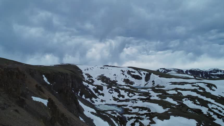 Snow covered mountainous terrain stretches to the horizon under heavily clouded sky