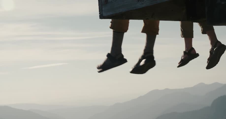 Two people dangle their feet over a pier overlooking a mountain