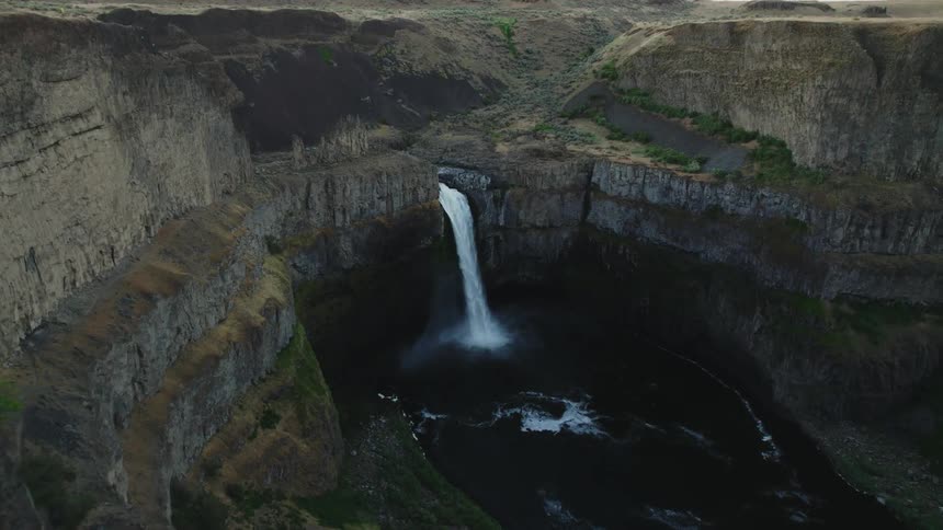 Aerial view of a strong waterfall pouring down a the rock face of a cliff on a lake in the mountains