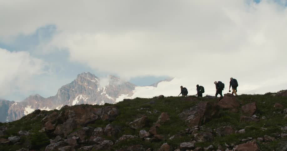 Four men hike across a cliff near a mountain range