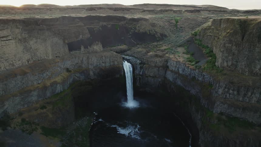 A waterfall gushes down from a canyon and into a natural pool below