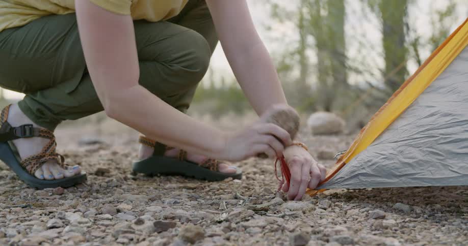 A woman is setting up a tent in the wilderness