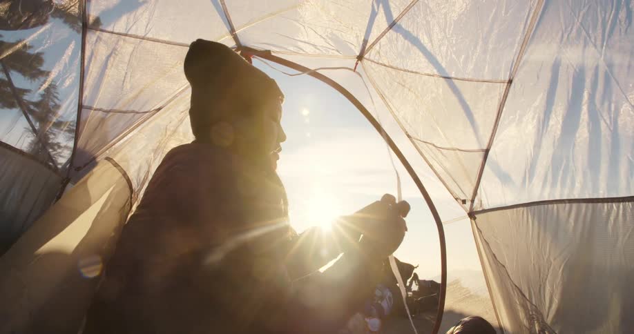 A woman is putting up a tent in the wilderness at dusk