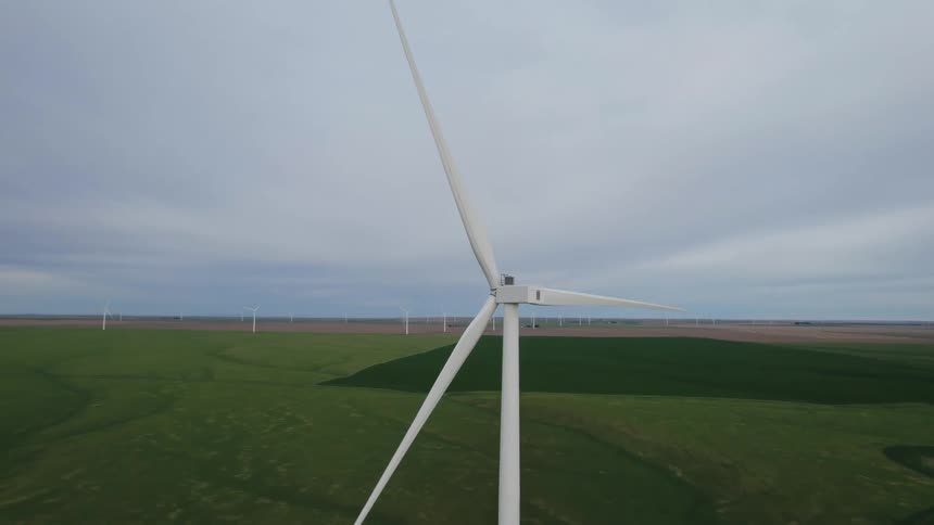 Wind turbines on a wind farm are spinning under a cloudy sky
