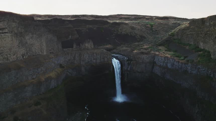 A waterfall rushes down the side of a canyon and into a river below
