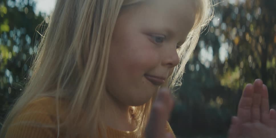 Two young blonde girls slap each others hands as they play a game outdoors on a sunny day