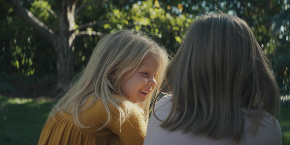 Two young girls sitting on the grass in the backyard at morning talking and smiling