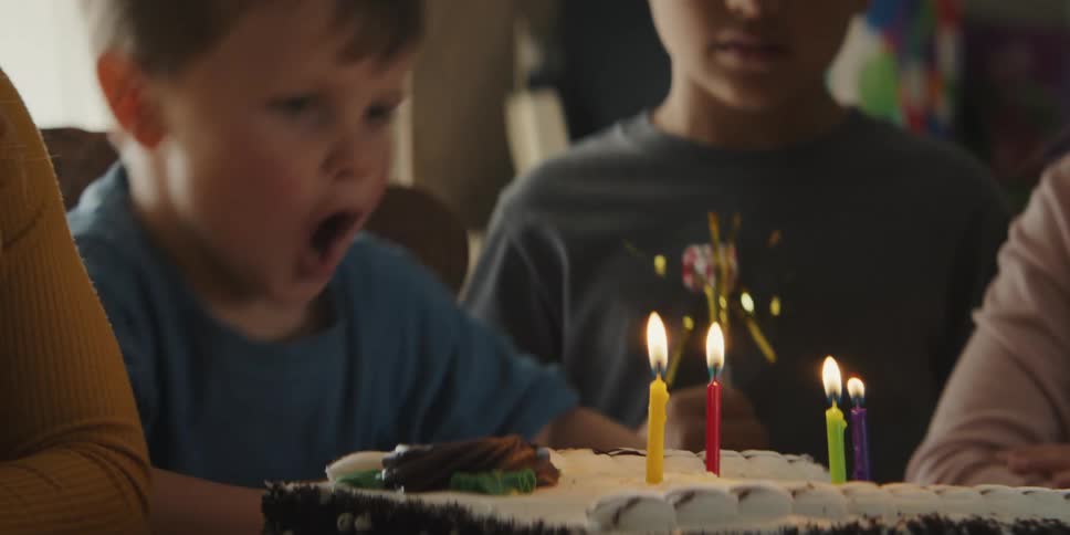 Boy in blue shirt blows out birthday candles amongst his friends
