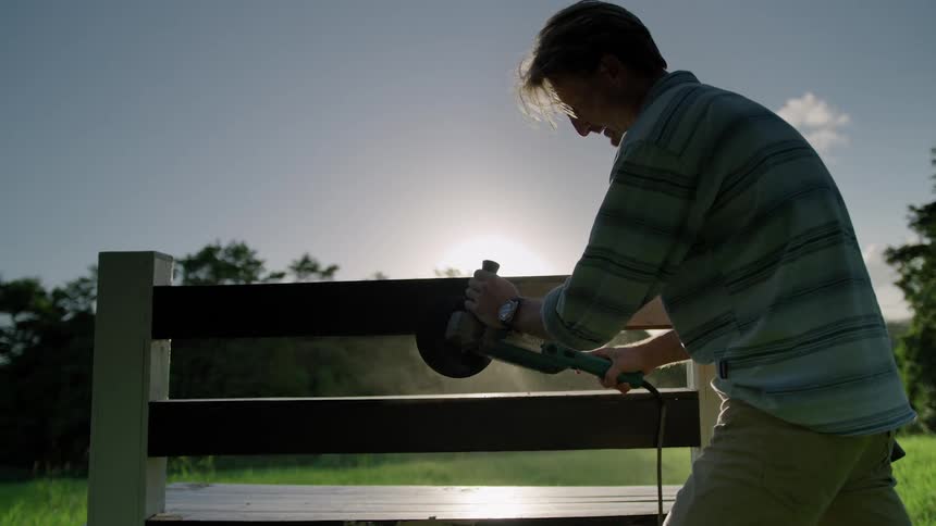 A man is outside using a power sander on a wooden fence