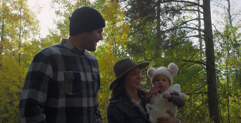 A woman holds her daughter while walking through the woods with her husband