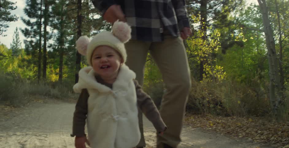 Father wearing gray plaid shirt brown pants and boots walks toddler son in the autumn forest