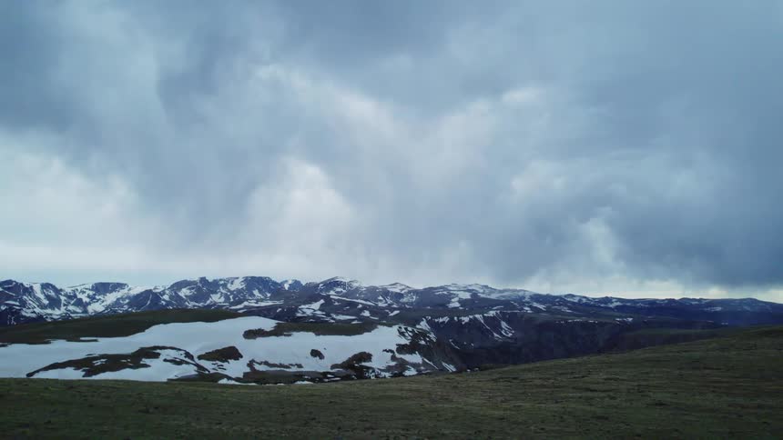 Aerial view of snowy mountain range under clouds seen from over hill