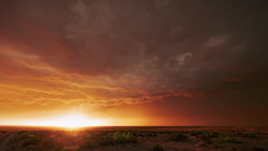 Clouds move across the sky as they reflect shades of orange and red from the sun rising on the horizon