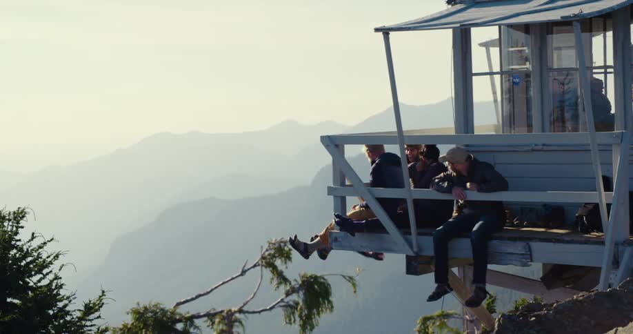 A group of friends sitting on the deck of a lookout tower with legs dangling and swinging