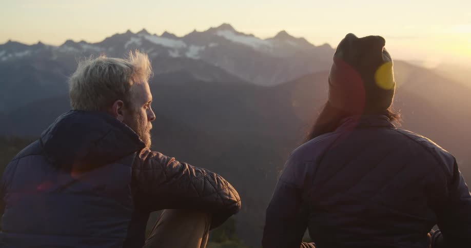 A man and woman talking while enjoying a snowy mountain view at sunset