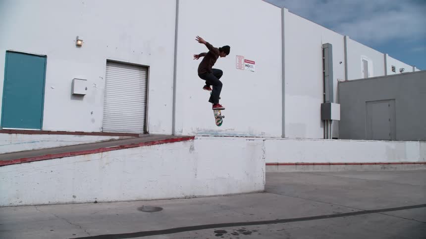 A man is skateboarding in an empty parking lot during the day