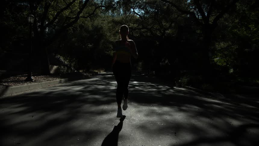 Woman runs down a tree lined street on a sunny day