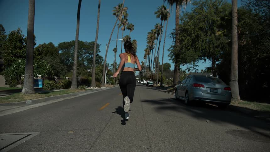 Woman jogging in the middle of street through residential neighborhood in slow motion