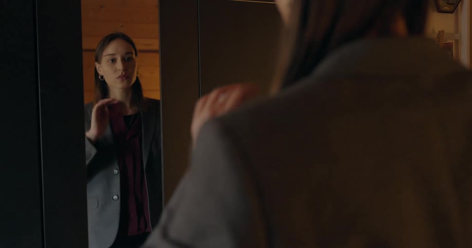 A woman checks her hair and suit jacket in a full length mirror