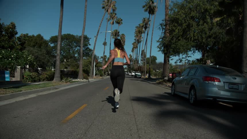 Woman with sports bra black leggings and white running shoes jogs on tree tunnel road in the street