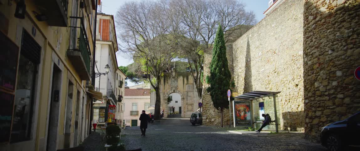 People walk on a village street and one person waits on a bus stop bench