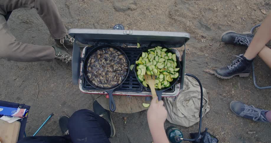 Overhead view of food in skillets cooking on portable grill outdoors while camping