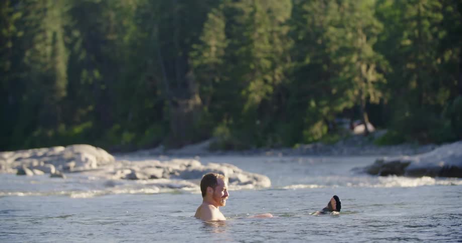 A man in swim trunks sitting down and floating in a forest river