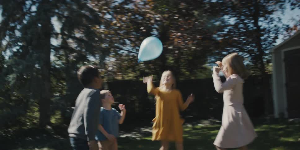 Children running and swatting a balloon on the lawn in the backyard