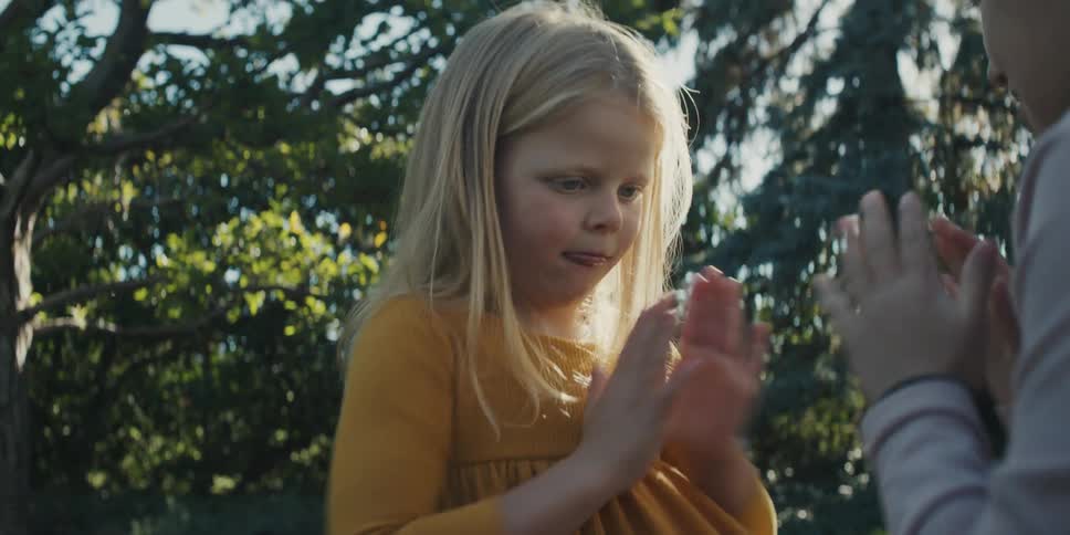 Two little girls sitting on the lawn playing patty cakes in the backyard